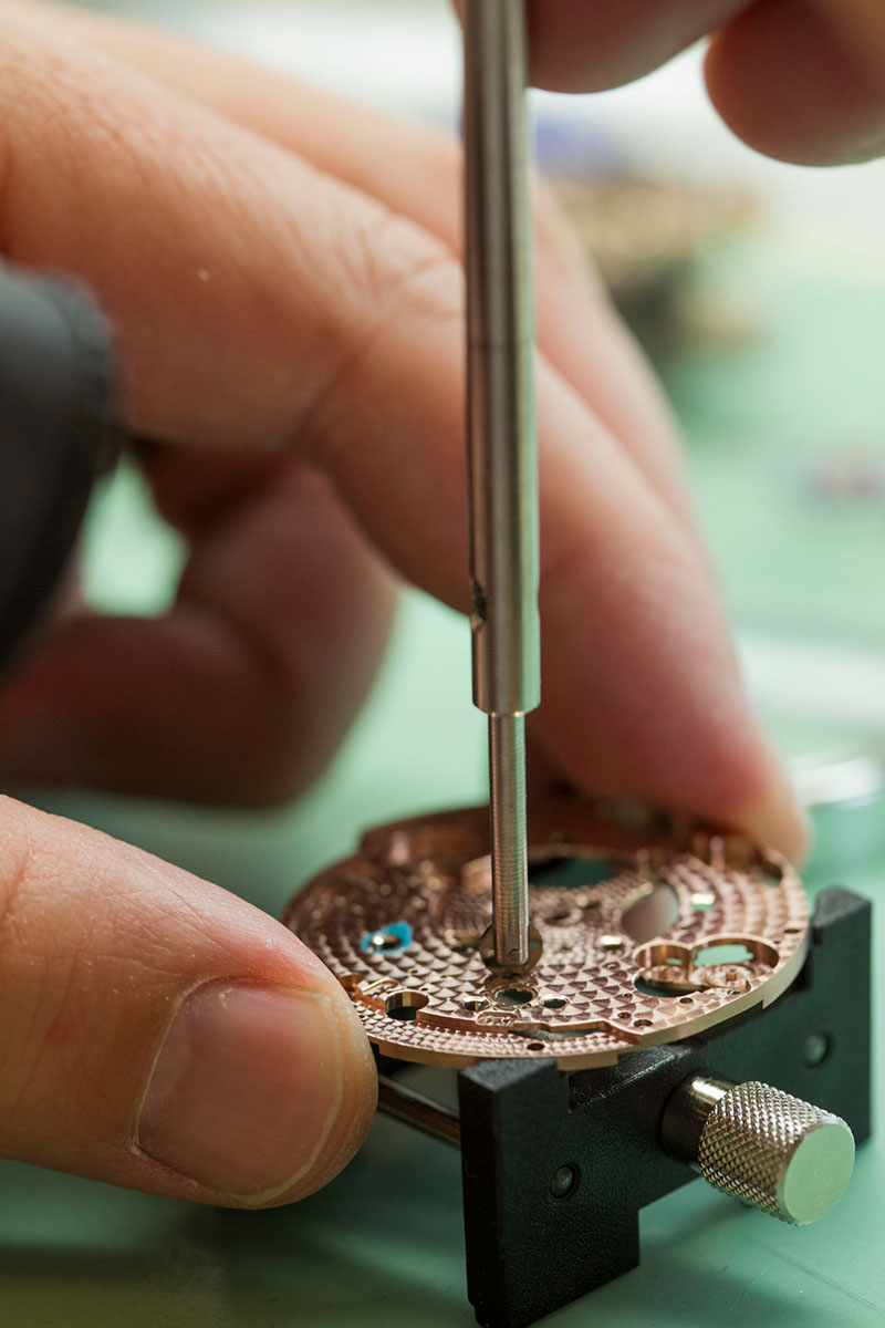 An Alchemists watchmaker working on the Cu29's movement hand stippled bottom plate